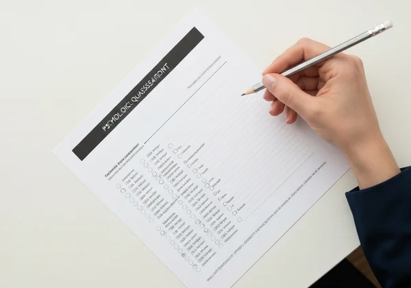 Bàn tay cầm bút chì trên một bảng câu hỏi tâm lý.